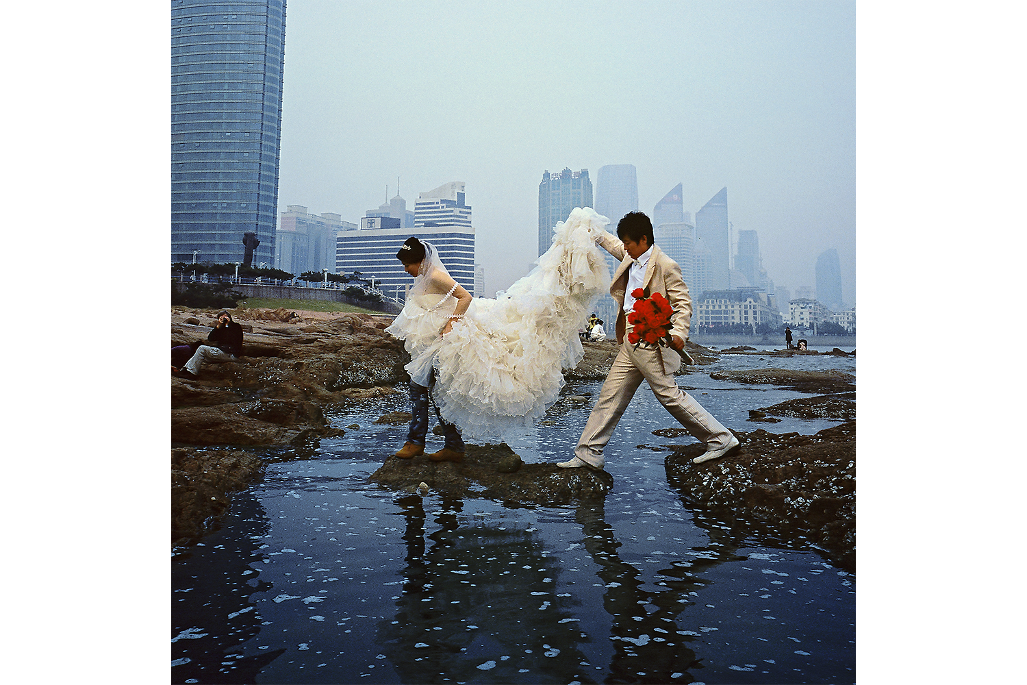 A couple dressed in wedding clothes tries to stay dry after a phots session in Qingdao. Photo by Chris Cherry @christophcherry