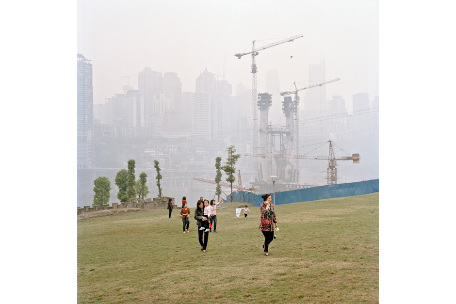 Construction cranes rise in the background mist as women walk with their children across the new grass of a development in Jiangbei. The city’s central business district is in the background.