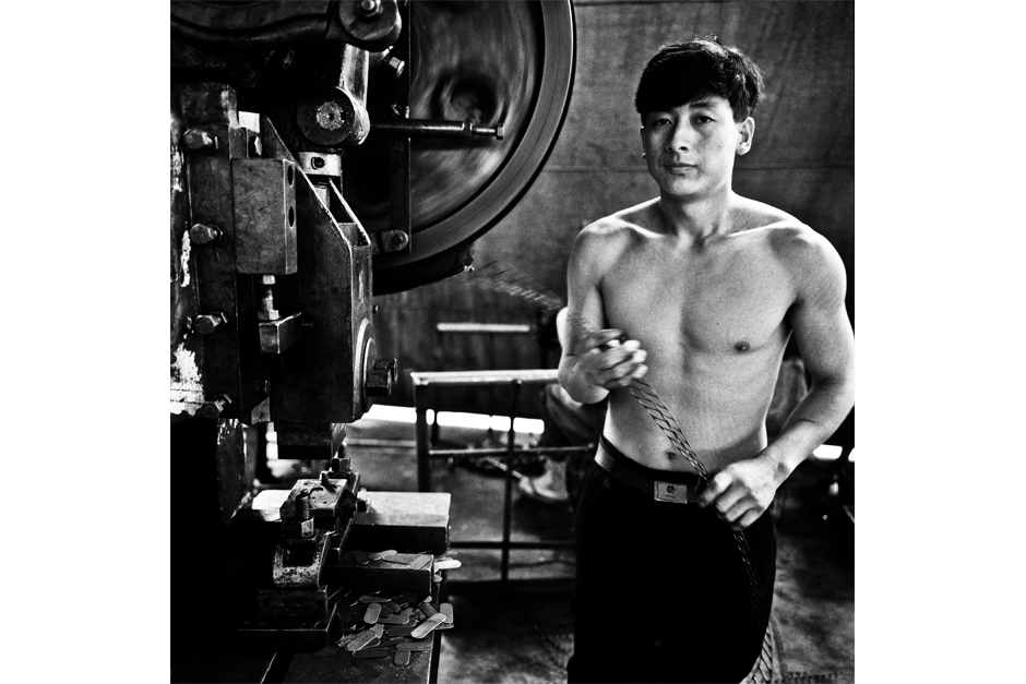 A worker pauses next to a metal punch machine that fabricates parts to attach to the carriage frames.