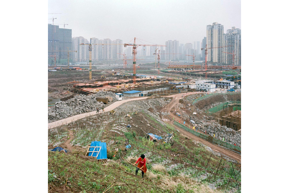 In the Jiangbei district, a woman cultivates a slope as giant cranes rise above a construction site for new housing and temporary structures used by the developers. With the influx of residents relocated from areas affected by the Three Gorges Dam, the Chongqing government began investing heavily in this part of the city, creating a new economic zone.