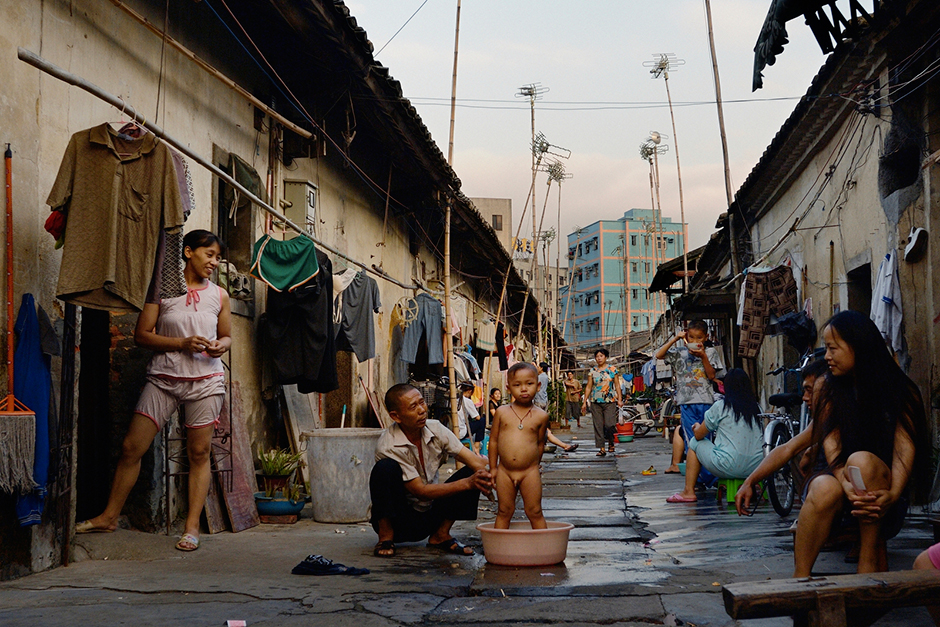 Xu Huali, left, moved to Shenzhen from rural Chongqing in 1991 with a grade school education. She eventually moved to Wuwucun in 1999 after marrying another Chongqing migrant. Xu has spent the last decade as a shoemaker. She currently glues soles to uppers for New Balance for 2,000 yuan (about $320) per month, but in 2005, she was earning much less making Reeboks. In this photo, taken on a rare Friday off from work, Xu watches her son, Zhao Neng, being bathed by his grandfather.