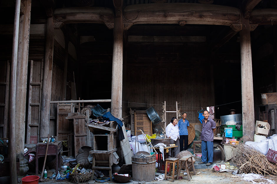 Wang Shouchang (right)  looks out at the main courtyard of Mingxian Hall with its caretaker, Wang Changfa (center), seventy-two, and his wife. Above the clutter, the elegant timbered roof beams remain intact. Wang Changfa began renting Mingxian hall from the government at 20 RMB per year in 1982. Since then, he and other villagers have gradually transformed the building into a communal storage space and barn for Wang Changfa’s pigs and chickens. “The government has long stopped charging me the rent,” Wang says,  “but I still have the responsibility to keep [the hall] standing.” 