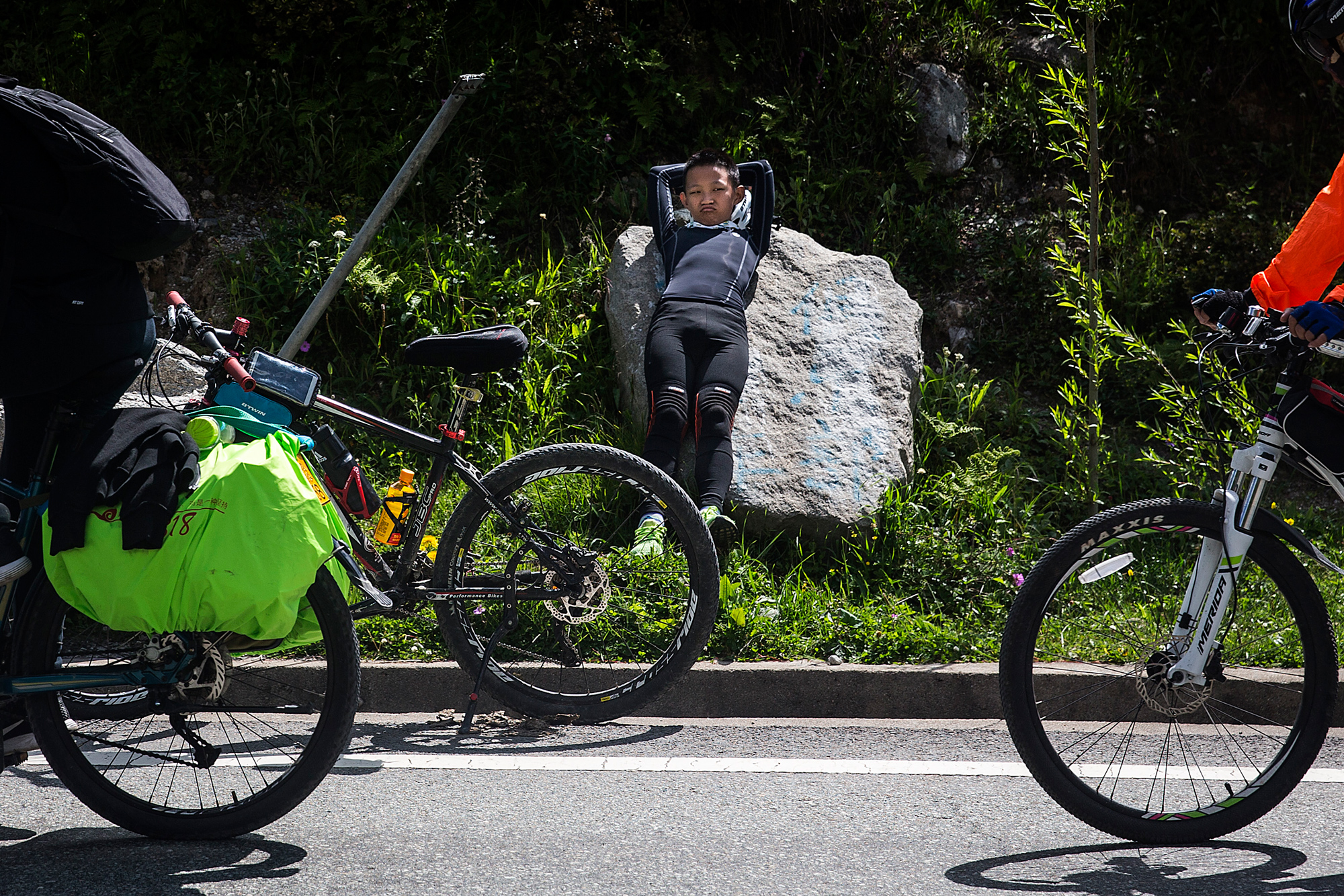 On the fifth day of the trip, Runxi rests on the side of the road because he is chafed from so many hours on his bike seat, in Zheduotang, Garze, Sichuan, July 19.
