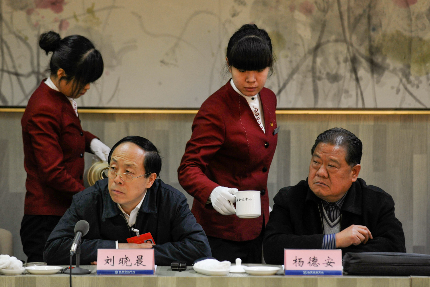 NPC deputies Liu Xiaochen (seated left) and Yang De’an listen to a speech by a Beijing deputy during a forum between NPC and Beijing Municipal People’s Congress deputies, as two female waitresses pass to refill tea, January 20, 2011.