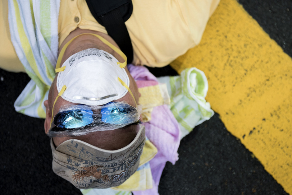 A man wearing a facemask and plastic wrap on his sunglasses sleeps at a pro-democracy protest on Nathan Road. (Photo by Alex Ogle/AFP/Getty Images)