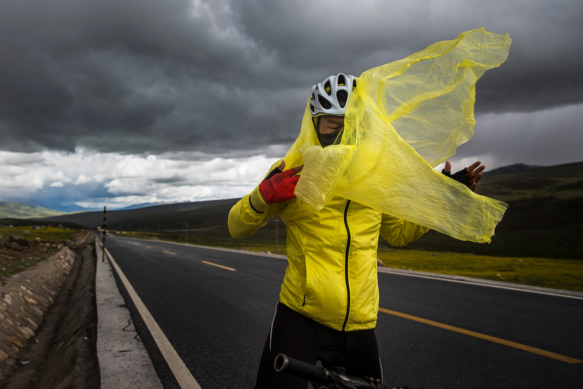 Chao puts on a poncho during a sudden rain and hail storm on Mount Haizi, elevation 15,000 feet, in Litang county, Garze, Sichuan, July 23.