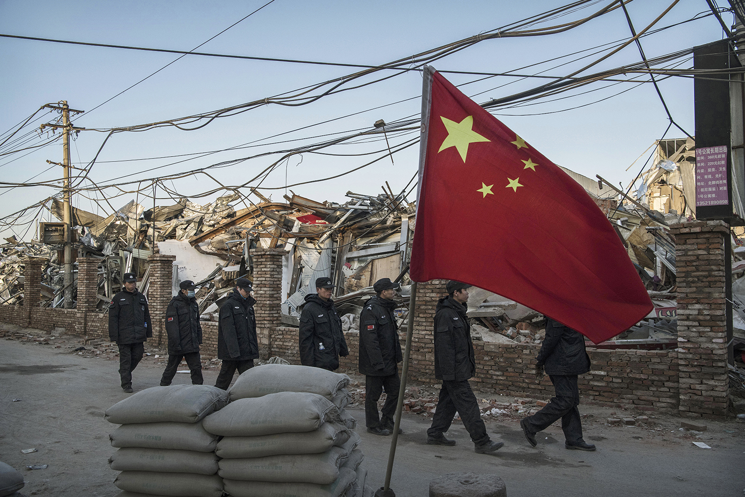 December 6, Chinese police walk in a line past houses and factories demolished by authorities in the Daxing District of Beijing. In recent weeks, thousands of migrant workers have been forcibly evicted in a sweeping government safety campaign following a deadly fire at a housing settlement. (Kevin Frayer/Getty Images)
