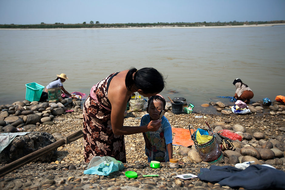 On the languid shores of the Irrawaddy River, a Burmese woman brushes <em>thanaka</em>, a traditional sunblock powder, on her son’s face after a mid-day bath. Though currently on hold, the Myitsone dam project threatens to alter life in riverside towns. The Chinese-financed hydroelectric project was suspended in September 2011 after years of public outcry.