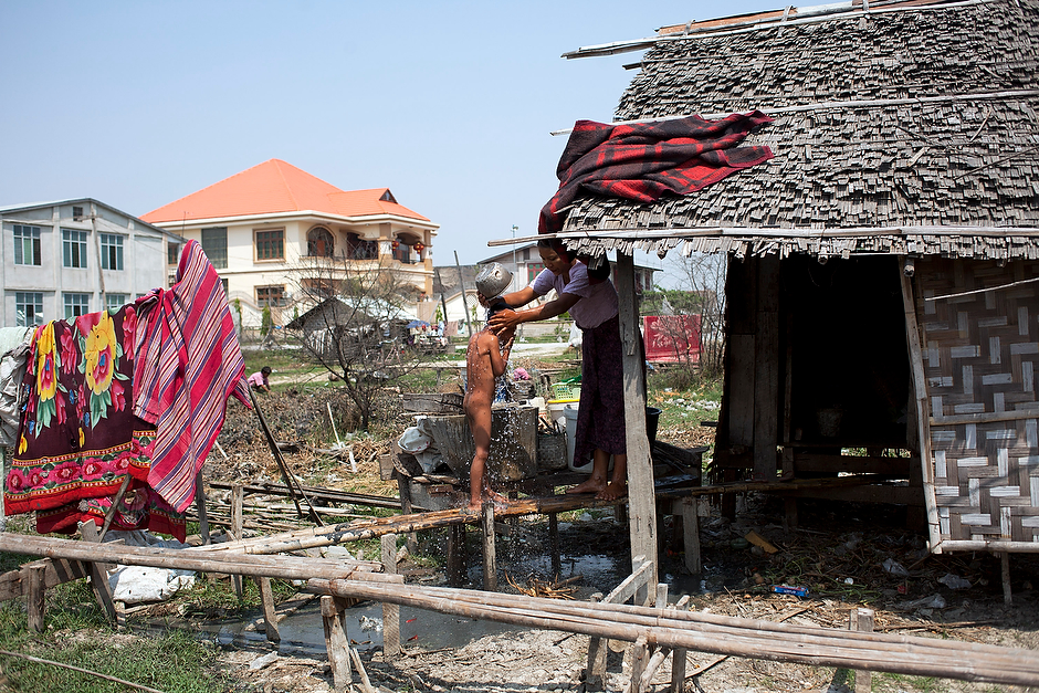 Ngwe Nyi Aye bathes her child, Naing Min Tun, 6, at their shack on the outskirts of downtown Mandalay, in view of a villa owned by a Chinese family.