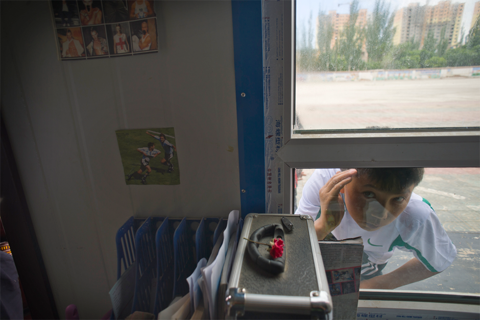 Dilmurat, who, like many Uighur goes by only one name, looks through a window while waiting for a friend. An outstanding goalie, Dilmurat has passed a qualifying test to the prestigious Evergrande Football School in Guangdong province, a requirement for acceptance. His father often drops by the school to watch him play.