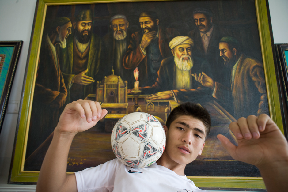 Imran, a young soccer player from Artux, poses in front of an oil painting in the school’s museum, which shows his ancestors debating the reform of traditional religious education. He recently spent a month in Italy training with the Juventus Football Club, and this is his first visit to Iksak, a place of great significance for Uighur soccer players.
