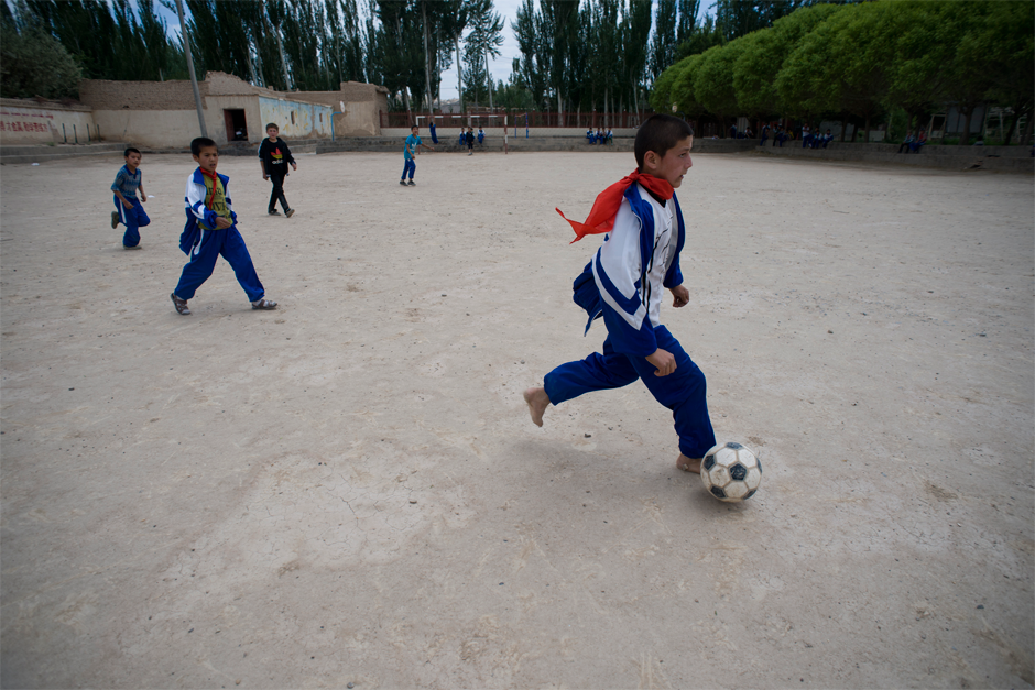 At an elementary school in Meyi Village, Azak Township, a student plays soccer barefoot on a dirt playing field.