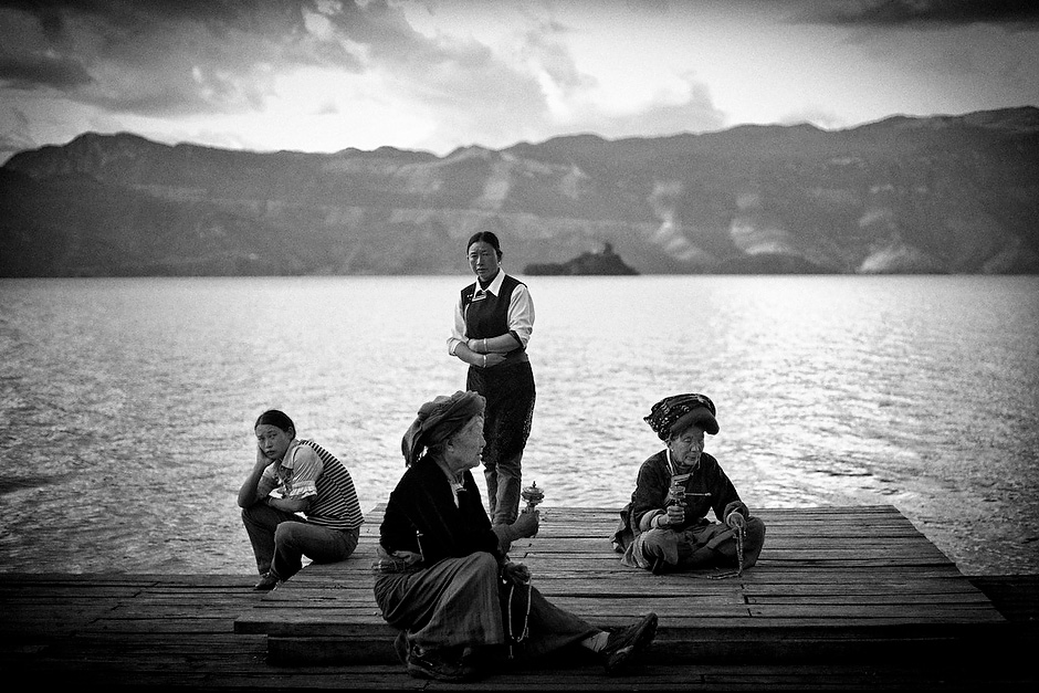 Mosuo women rest by Lugu Lake, some spinning prayer wheels. Despite the development around Luoshui, Mosuo women continue their traditional way of life, emphasizing a culture revolving around large matriarchal families and practice of Tibetan Buddhism. Luoshui, Yunnan, China.