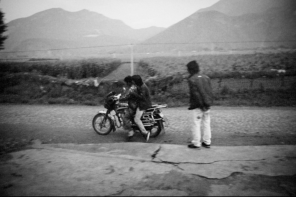 Young men gather outside the only provision shop at dusk before heading to their “walking marriages.” These days, men whose partners live too far to walk typically ride motorcycles instead. Zha Xi, 22, heads off to the hot springs before seeing his lover. Aguwa, Yunnan, China.