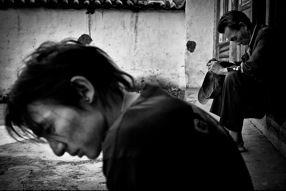 Su Na finds village life boring, but working in cities has proven to be an even greater struggle. In the background, a relative from Lugu Lake comes to visit his wife and children in Aguwa. Aguwa, Yunnan, China.