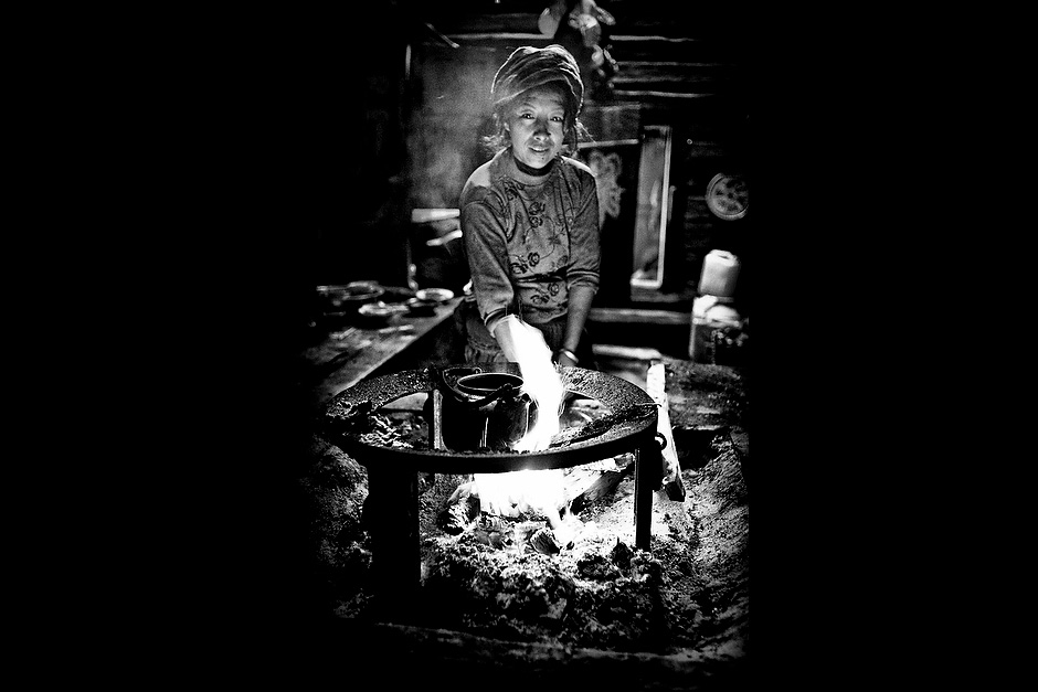 Ci Er Zu Ma, 40, wife of Song Nang Da Zhu, 49. The Mosuo life revolves largely around the hearth, which is used for cooking, warming up, and smoking. Wujiu, Sichuan, China.