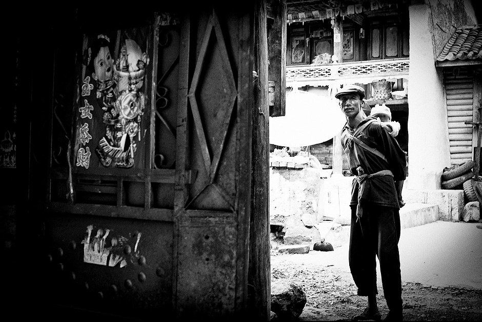 Da She, 59, carries his granddaughter, 2, while everyone else in the household is busy. Aguwa, Yunnan, China.