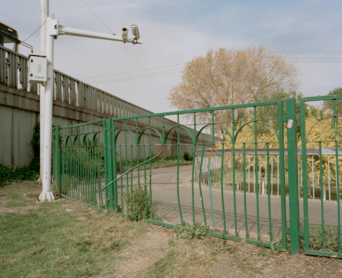 A surveillance camera mounted above a broken fence overlooks a park in Urumqi, May 2016.
