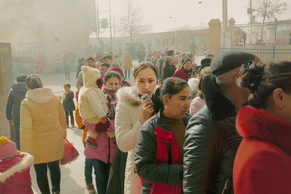 Uyghur residents wait in line at an ID and body search checkpoint before entering the local bazaar, in Hotan, February 3, 2019.