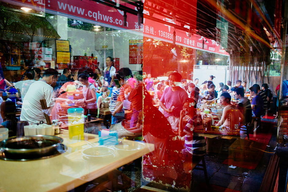 Crowds seated indoors blend with those outdoors in a window reflection at Gang Shan Zhazha, a popular street-side hotpot restaurant on Tiyu Road.