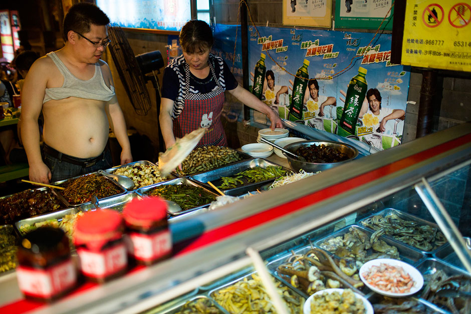 Workers serve small plates of snacks to people eating at Old Home Kitten Noodles (Lao Difang Mao’er Mian) near Ciqikou, an ancient town dating back to the Ming Dynasty. These snacks are usually consumed while drinking beer. The restaurant is primarily outdoors and is open 24 hours a day. Ciqikou is a major tourist destination in Chongqing, but at night the tourists disappear and locals come out to eat from street food vendors.
