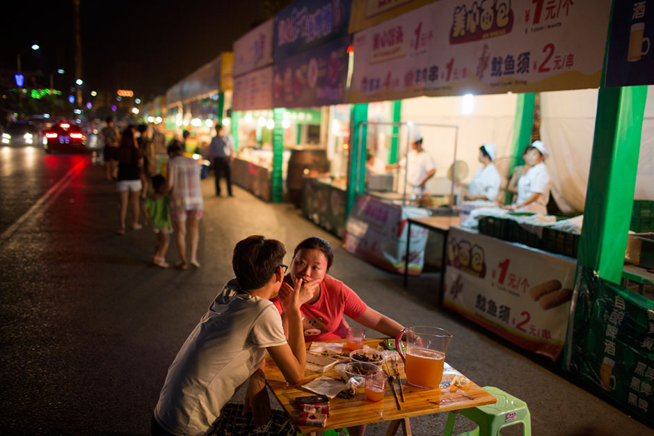 A couple eats lamb and chicken skewers and drinks beer from a food stall near the carnival on Meixin Foreigner Street, a sprawling amusement and oddity park in northeastern Chongqing. The park is popular among working-class Chongqingers. Meat skewers cost 1 RMB each.