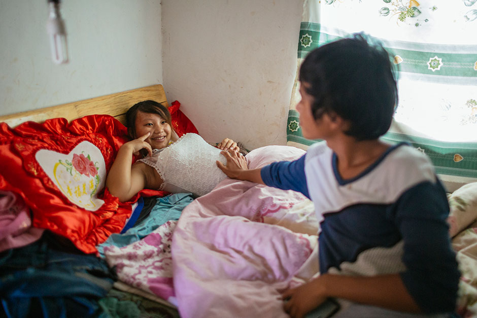 Wen touches his wife Jie’s pregnant stomach. He is 18 and she is 13 years old. They live together in Tangzibian village, Mengla county.