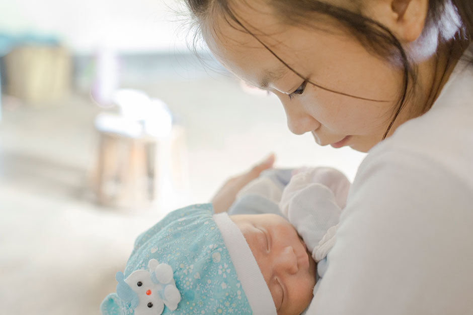 Cai, 16, holds her two-month-old son at home. A year earlier, she married and dropped out of school when her family could no long afford to pay for her education.