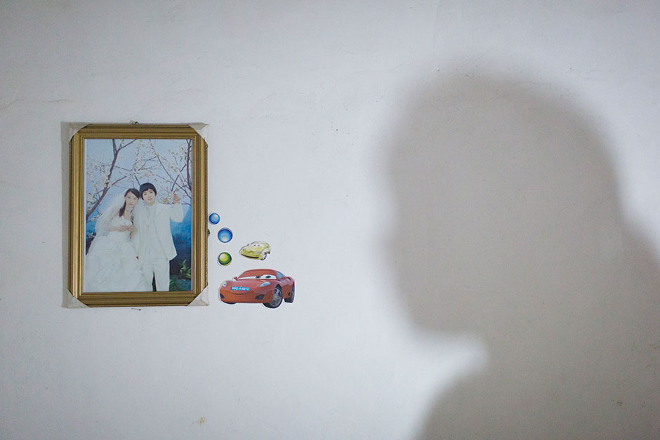 Jie’s shadow falls across her bedroom wall near her and her husband’s wedding photo. At age 13, Jie was six months pregnant. Her husband is five years older than her.