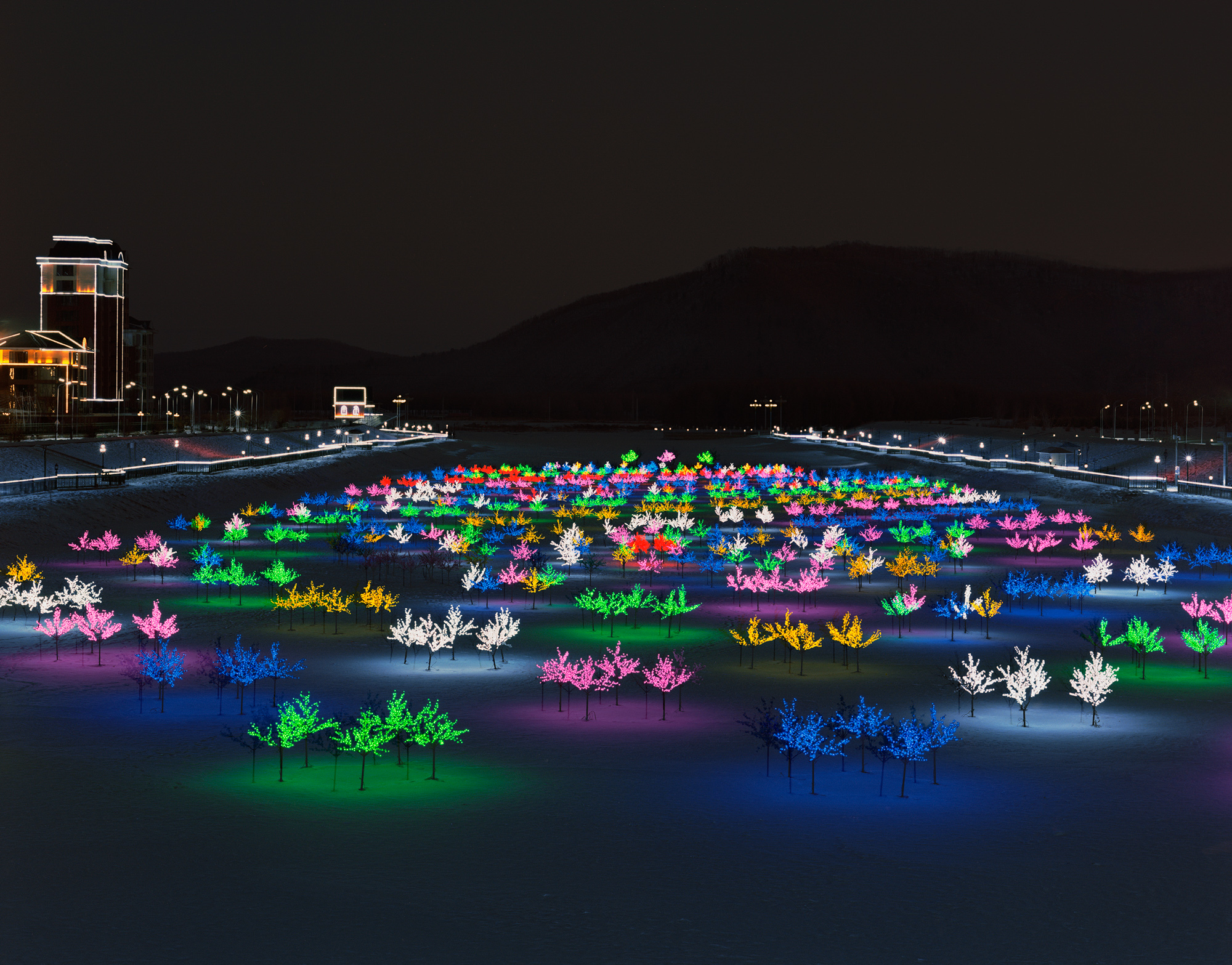 Plastic trees with colorful light bulbs glow on a frozen river in Yichun.